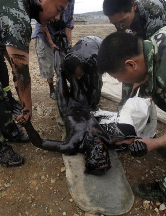 In this photo released by Greenpeace, a firefighter submerged in thick oil during an attempt to fix an underwater pump is brought ashore by his colleagues in Dalian, China on Tuesday.